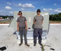 HVAC Blog 5 Two technicians standing beside a rooftop HVAC unit on a clear day.